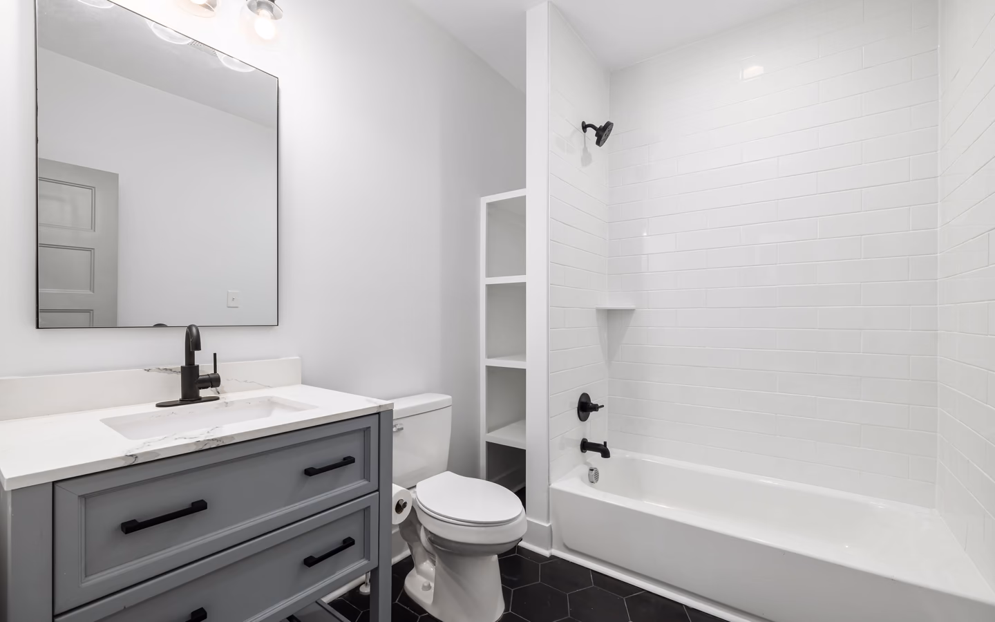 Modern bathroom with a white tub, hexagon tile, black accents, and a compact vanity