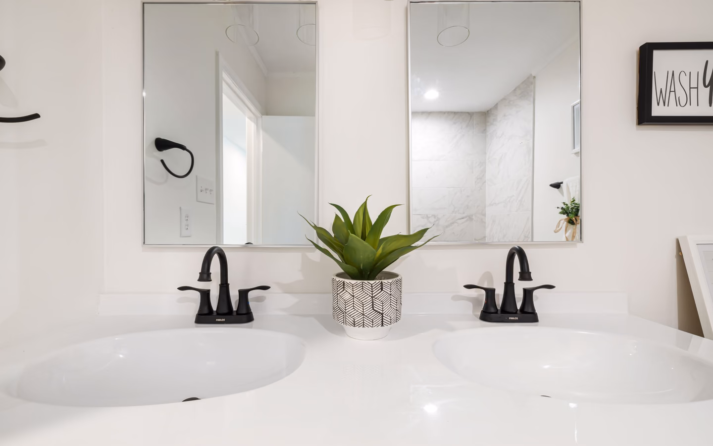 Modern double vanity with black faucets, white counters, and a geometric plant pot