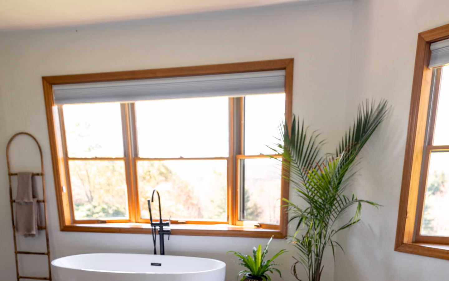 Organic modern bathroom with a freestanding tub, warm wood floor, and leafy plants by the windows