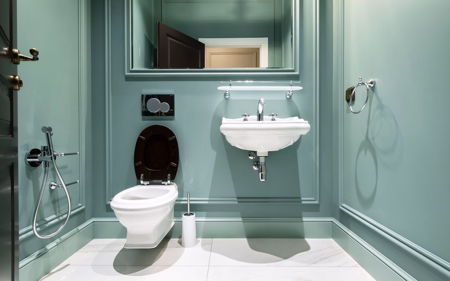 Tailored green powder room with paneled walls, a wall-mounted sink, and polished chrome fixtures
