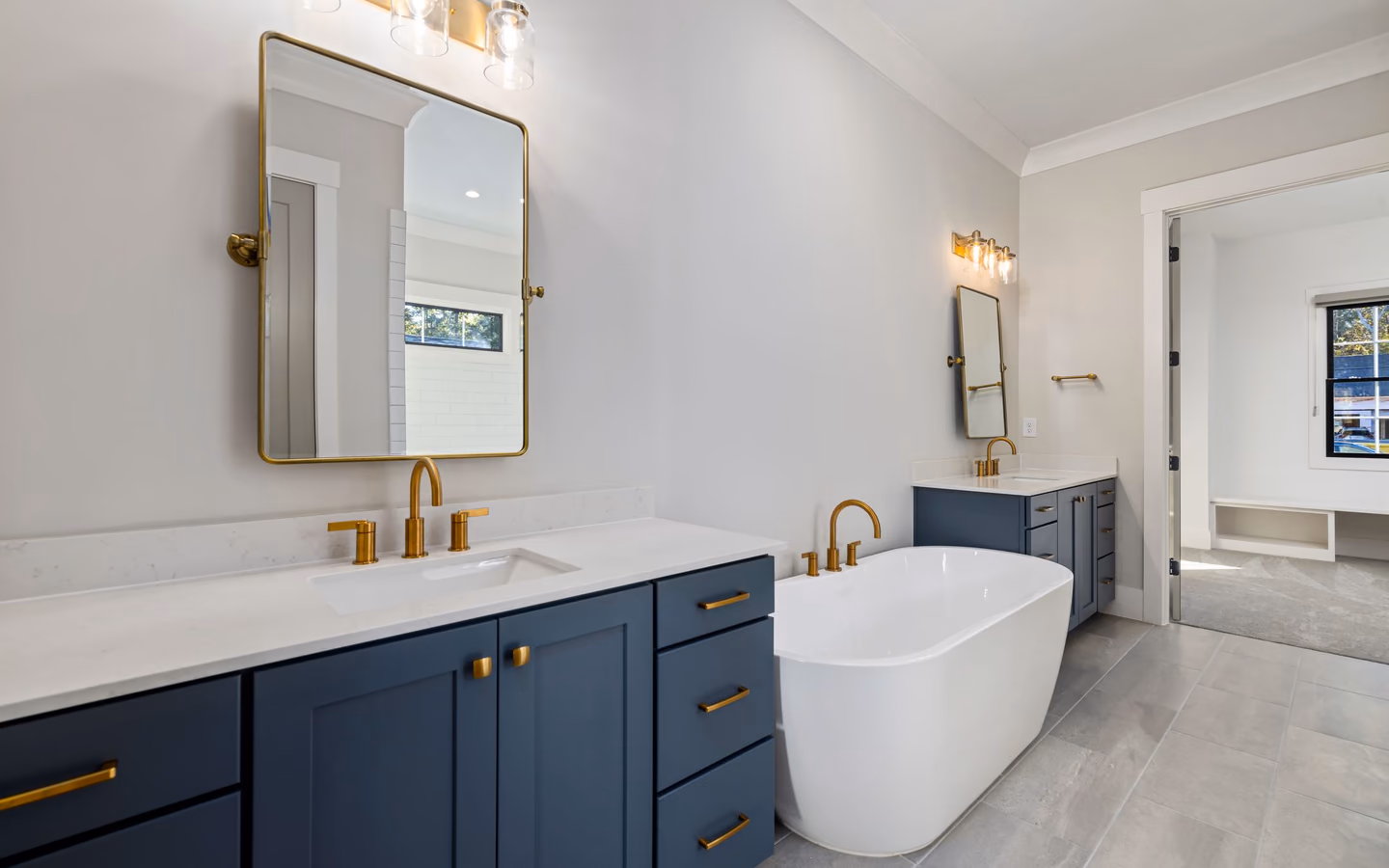 Polished contemporary bathroom with a freestanding tub, blue double vanities, and warm metal fixtures