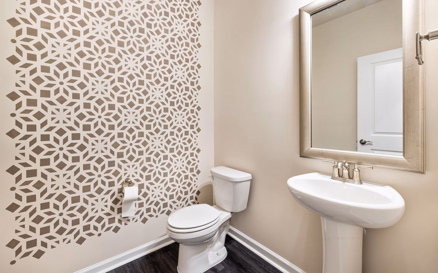 Compact powder room with a geometric accent wall, pedestal sink, and framed mirror