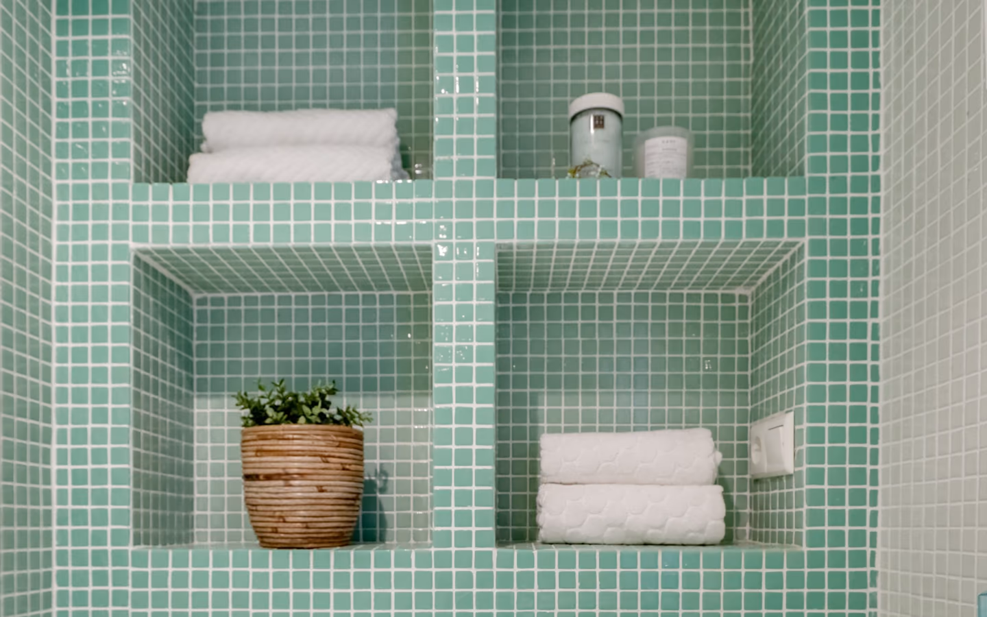 Modern bathroom wall with rich green tile, recessed shelves, and a white basin