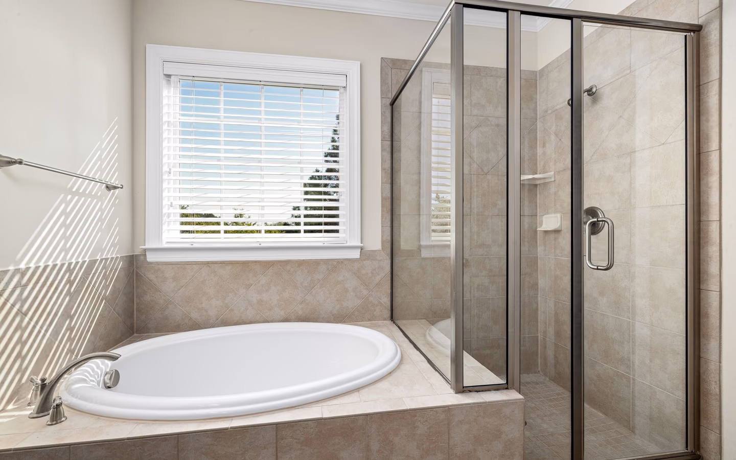 Sunlit bathroom with a glass shower, freestanding tub, and calm neutral finishes