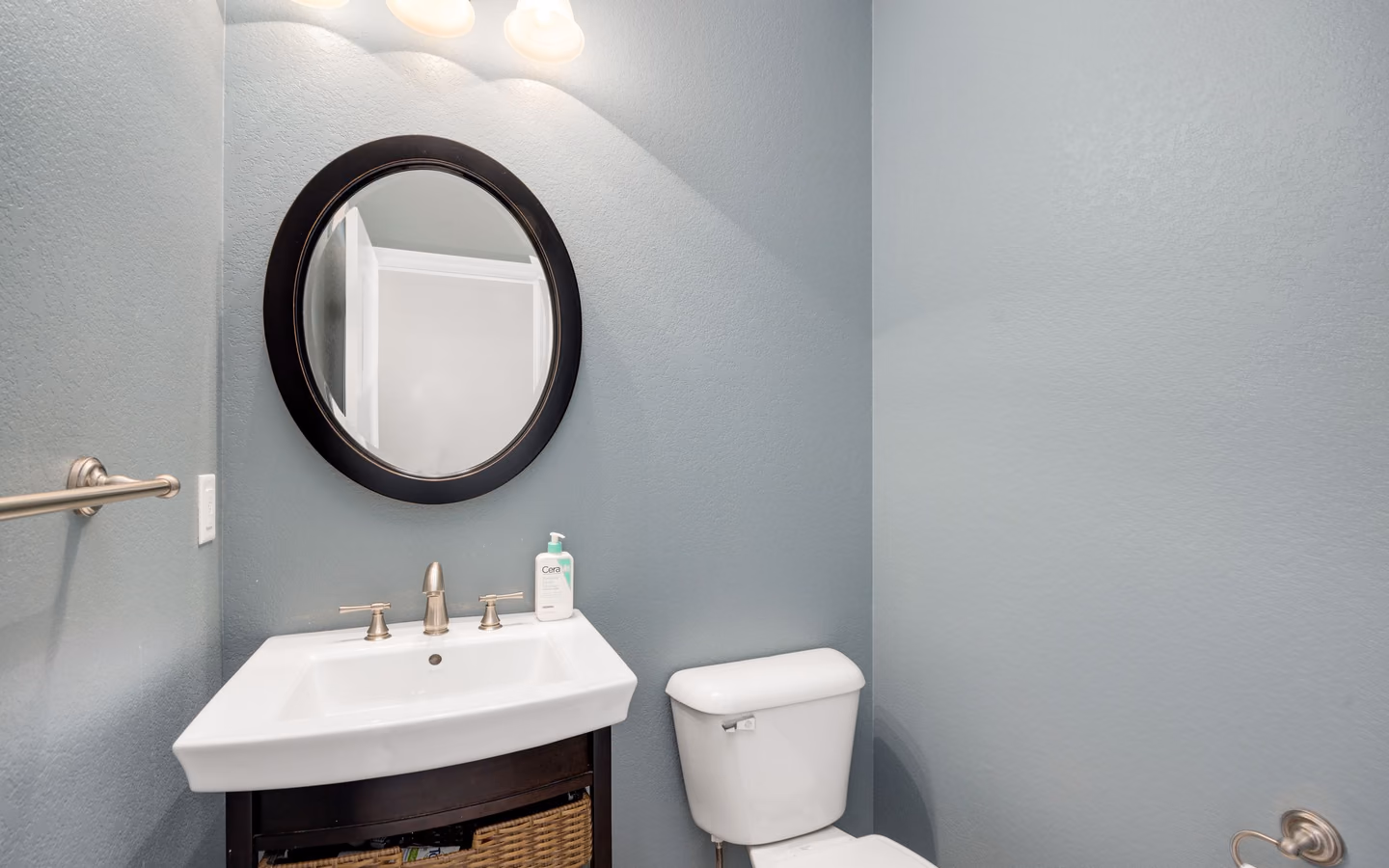 Compact gray powder room with a small vanity, round mirror, and open basket storage