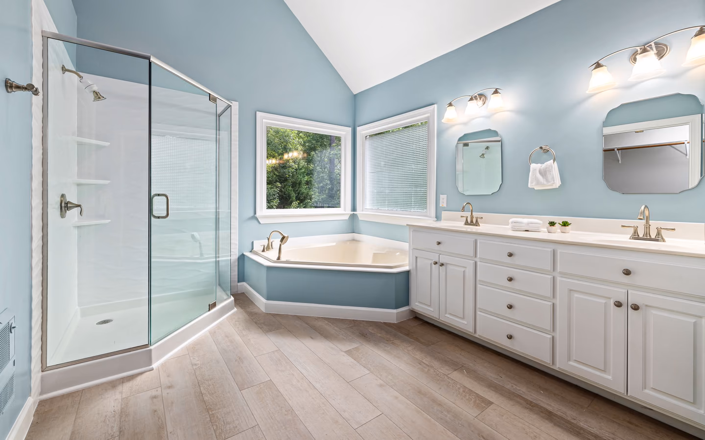 Elegant blue bathroom with a glass shower, corner bathtub, and dual-sink vanity