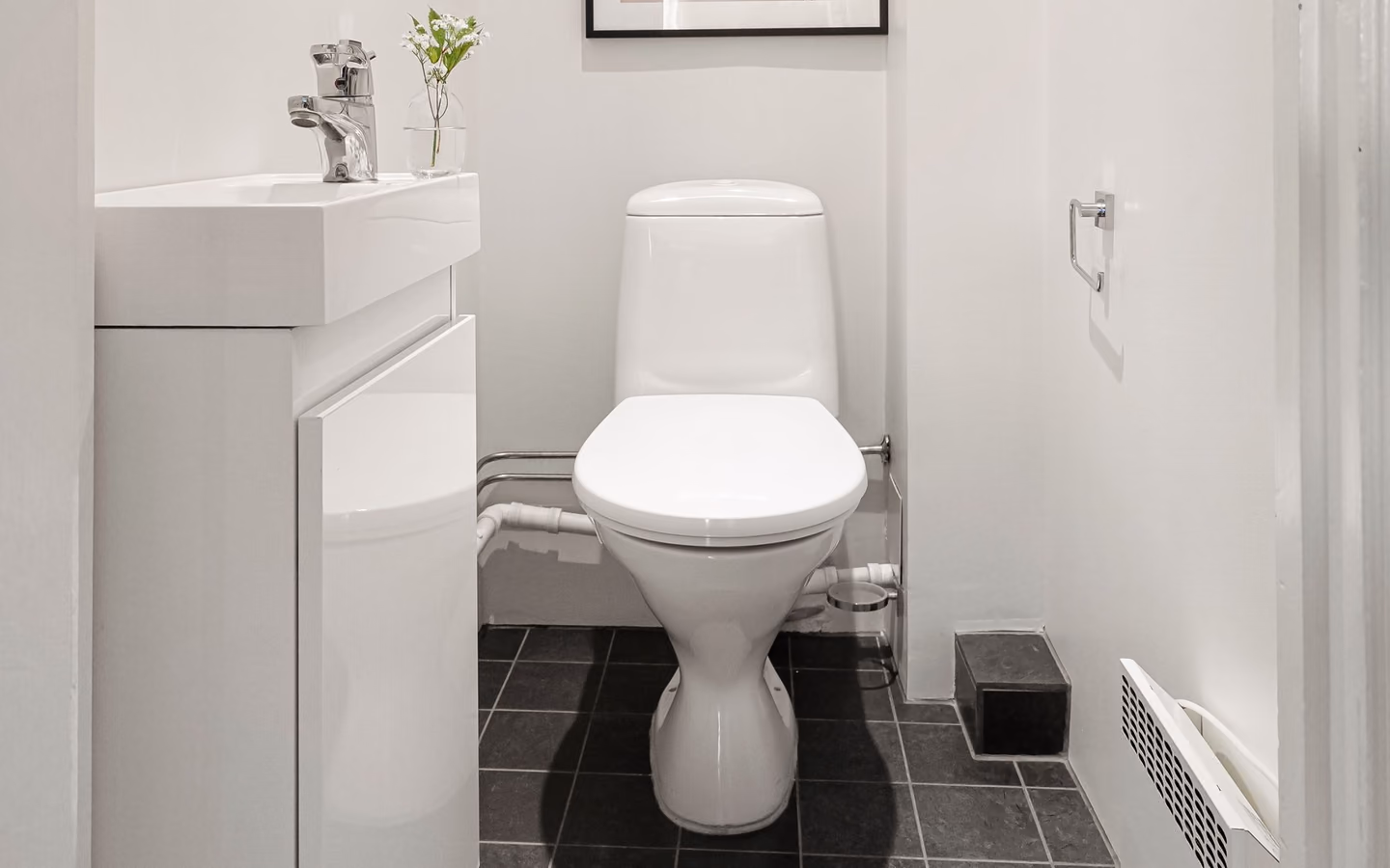 Narrow minimalist powder room with a compact vanity, black tile floor, and framed artwork