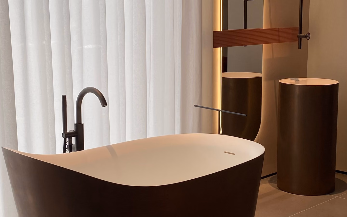 Sculptural dark freestanding tub in a restrained modern bathroom with smooth concrete walls