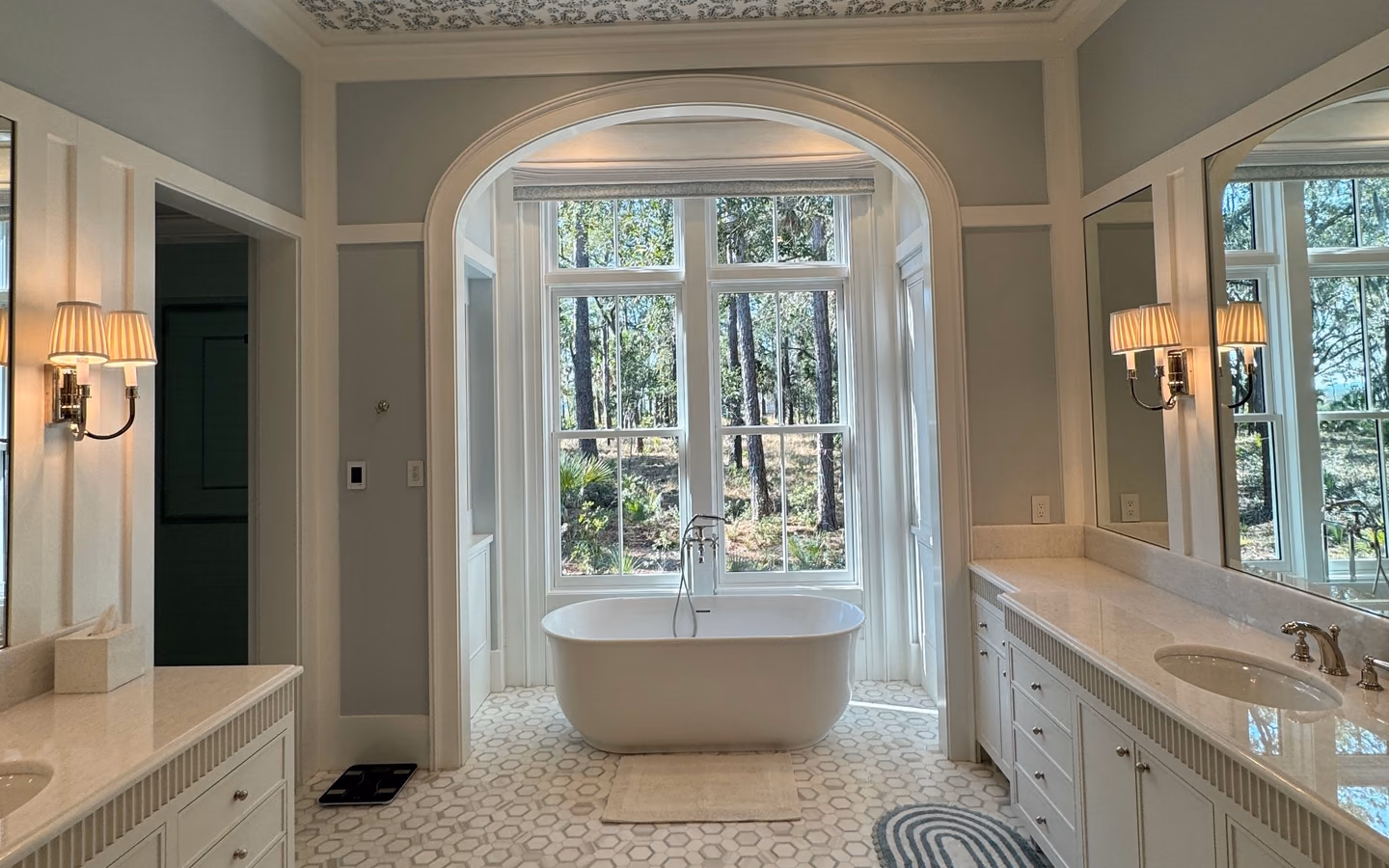 Luxury bathroom with a freestanding tub, long vanity, patterned floor, and curved window