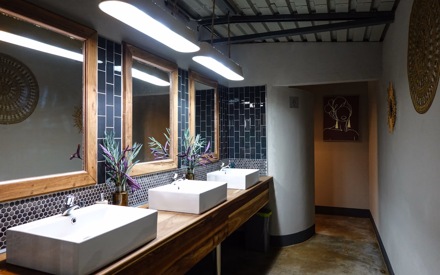 Contemporary bathroom with a wood vanity, plants, mirrors, and warm layered lighting