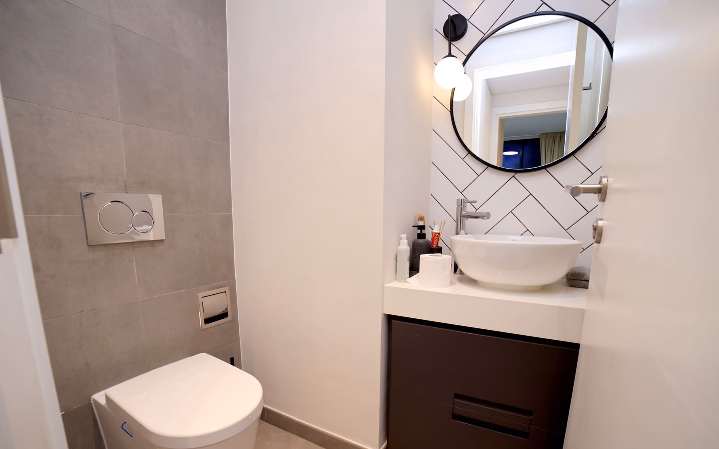 Renovated minimalist bathroom with a streamlined vanity, round mirror, and warm lighting