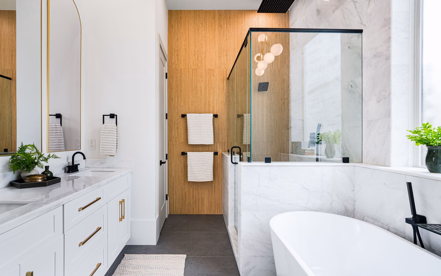 Organic modern bathroom with a freestanding tub, warm wood millwork, and a glass shower