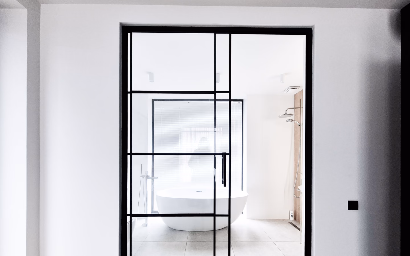 Bright minimalist bathroom with a freestanding tub and black-framed glass wall