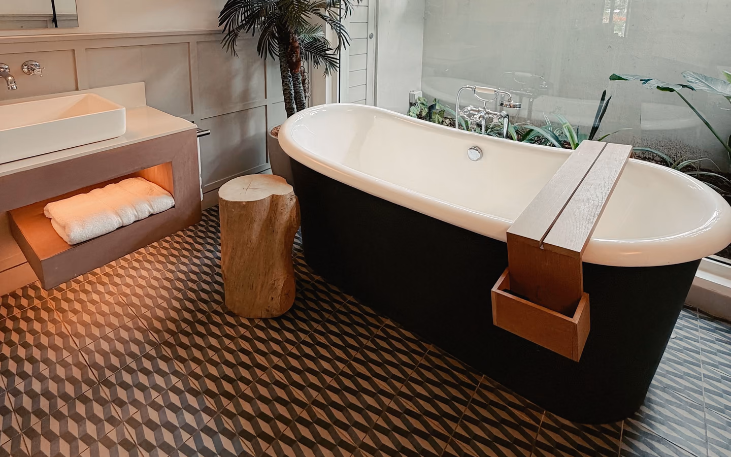 Organic modern bathroom with a freestanding tub, natural wood accents, warm stone, and tropical greenery