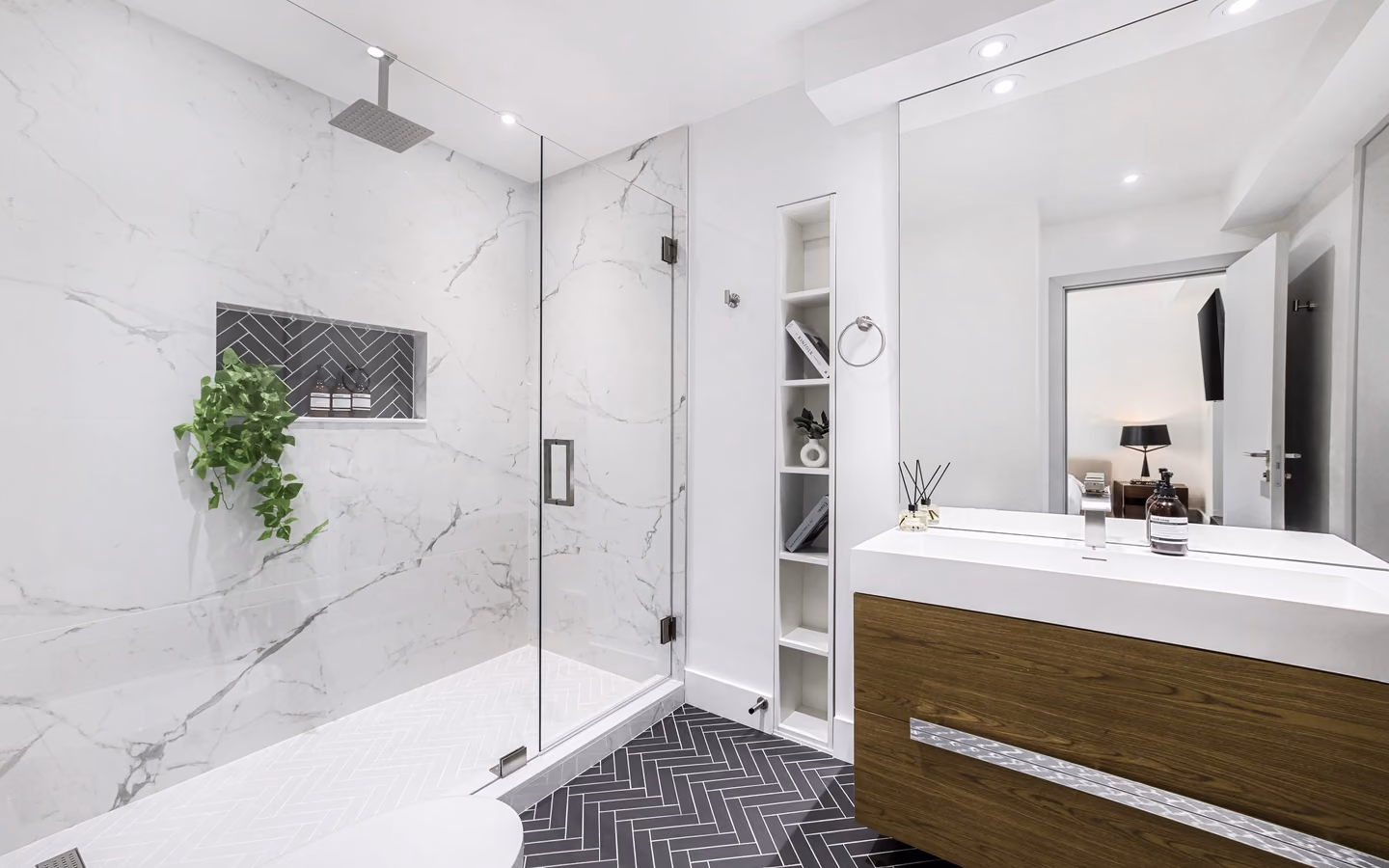 Wide modern bathroom with a wood vanity, marble shower, and herringbone flooring