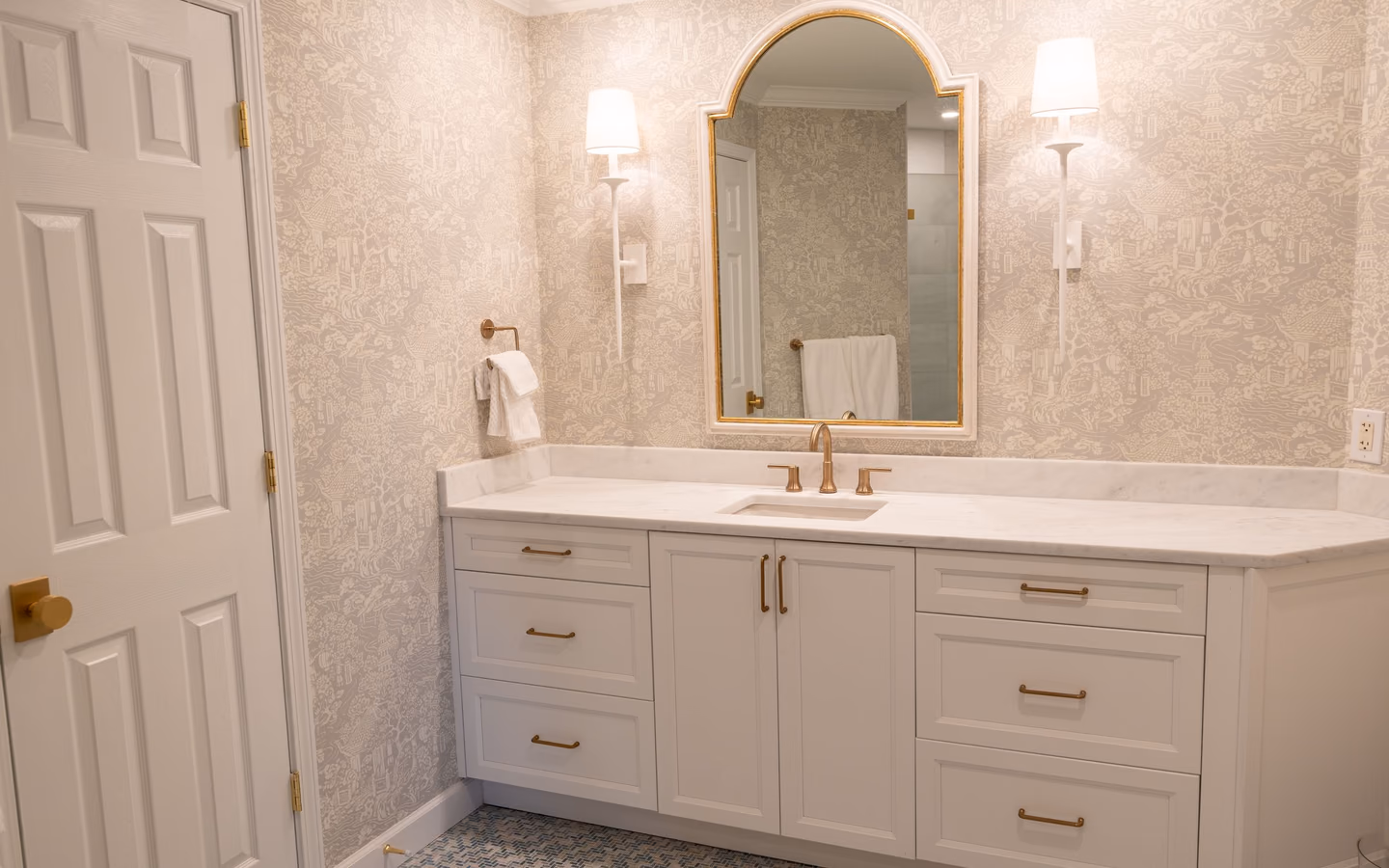 Bright powder-room vanity with tailored cabinetry, patterned wallcovering, and warm metal details