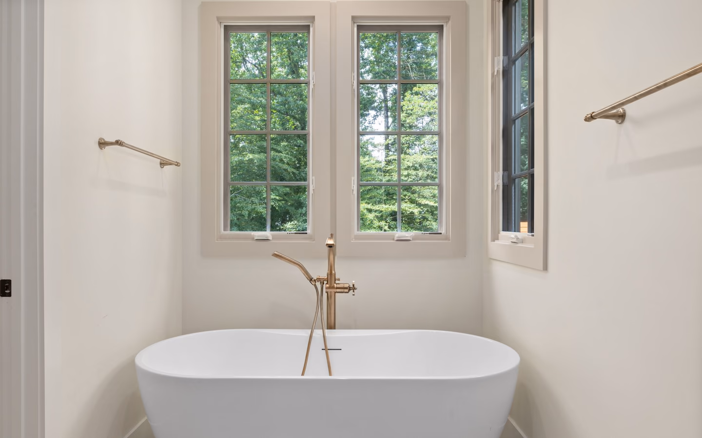 Calm spa-inspired bathroom with a freestanding tub, tall windows, and restrained warm metal fixtures