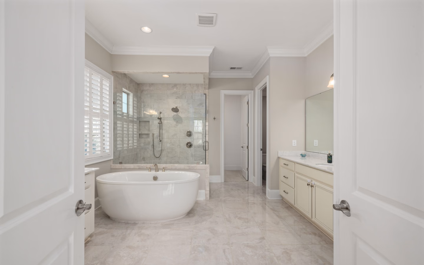 Bright modern bathroom with a freestanding tub, glass shower, and tailored white vanities