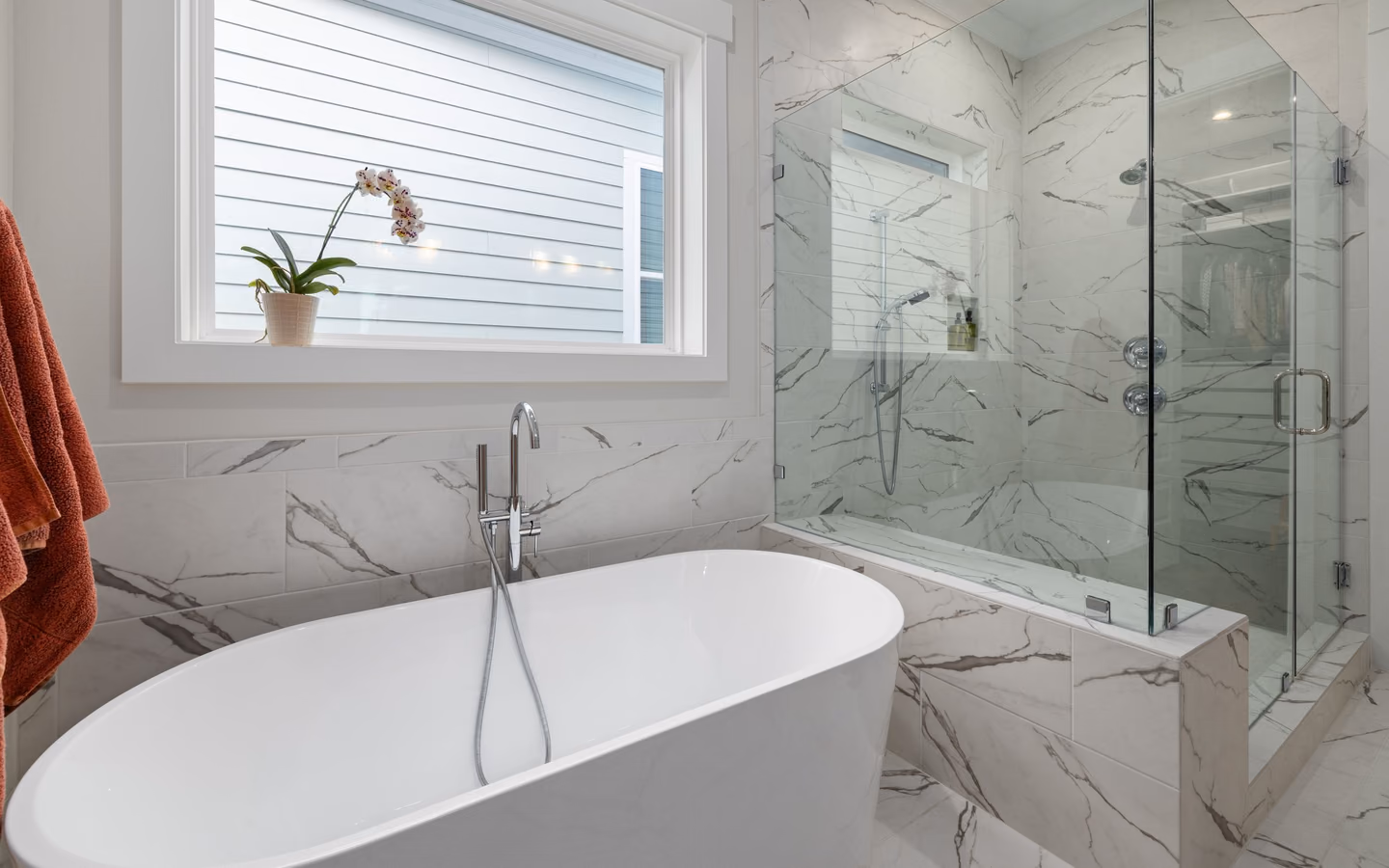 Modern marble bathroom with a freestanding tub, glass shower, and natural light