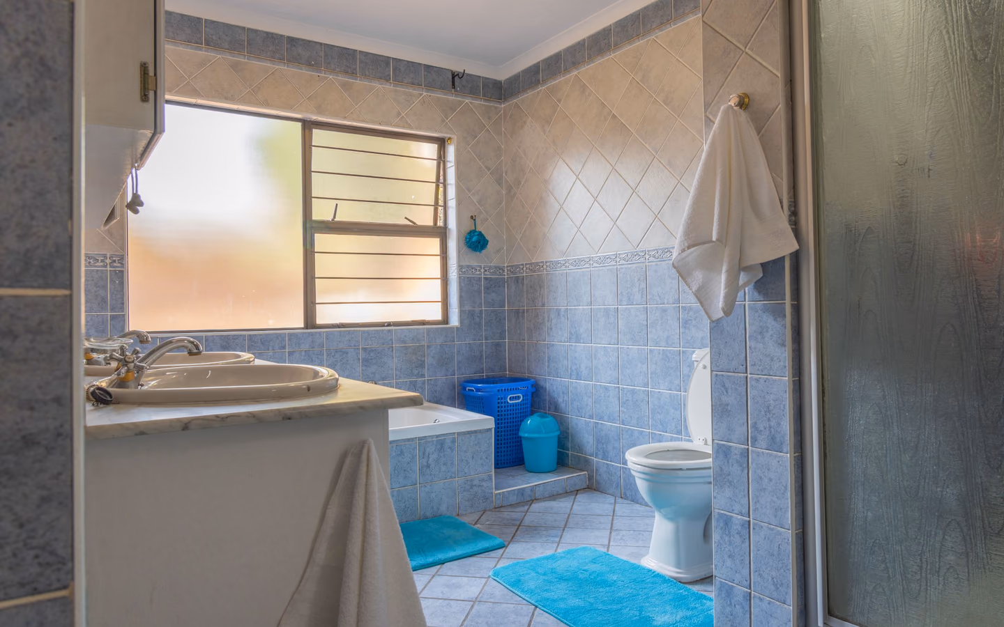 Blue tiled bathroom with white fixtures and natural light through a frosted window