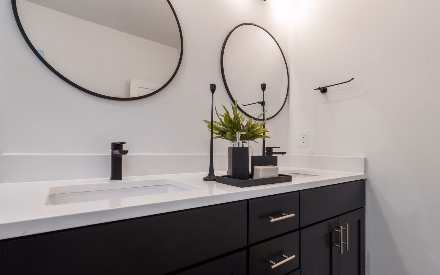Black and white double vanity with round mirrors, black faucets, and clean-lined cabinetry