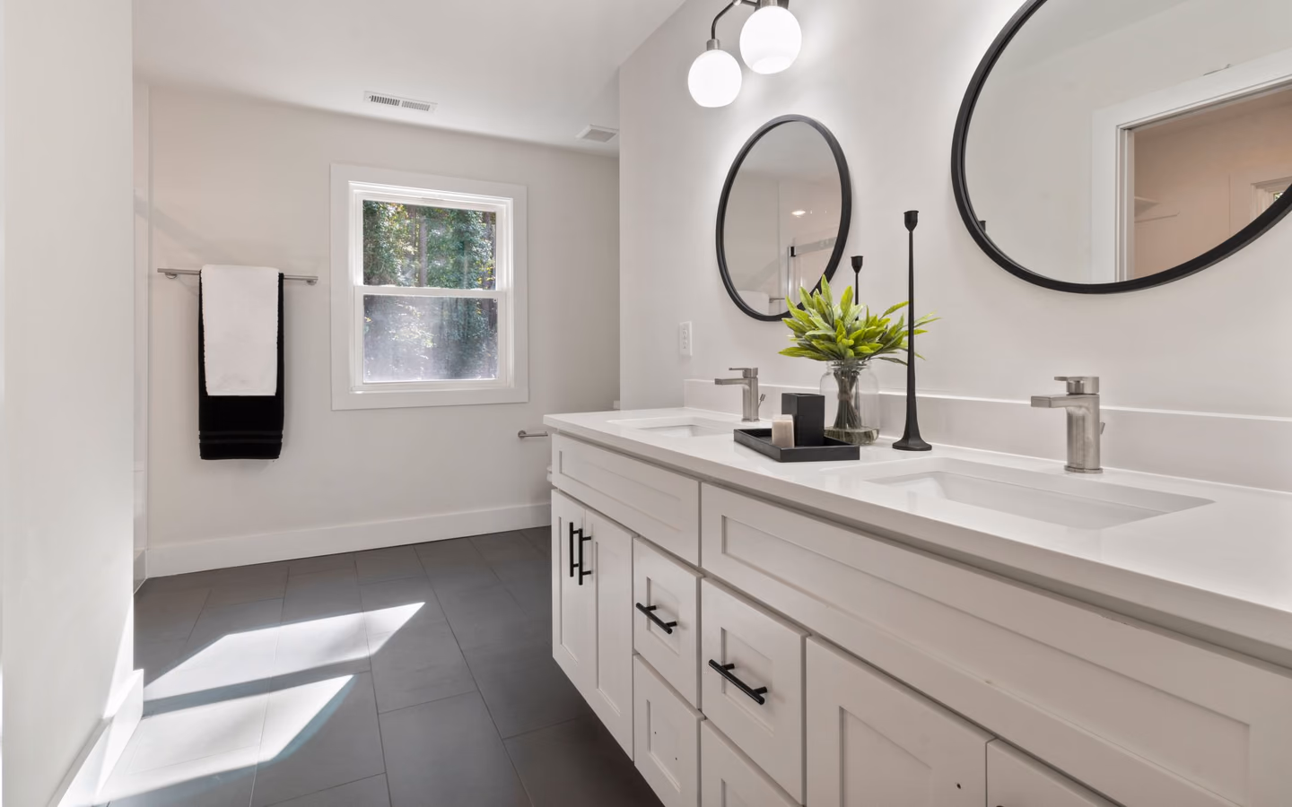 Bright bathroom with a white double vanity, round mirrors, and fresh green accents