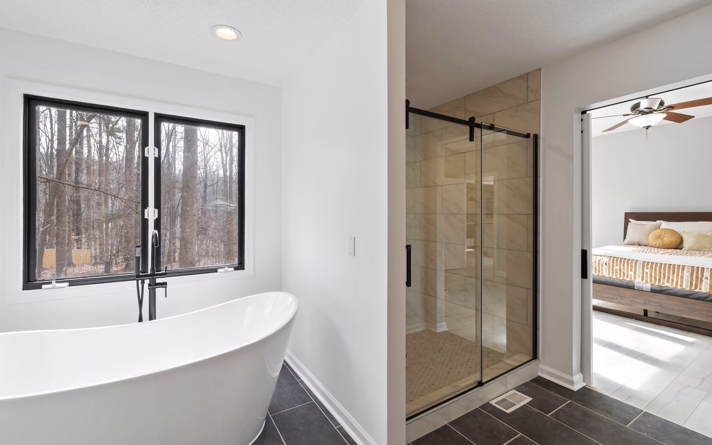 Serene bathroom with a freestanding tub, glass shower, black-framed windows, and wooded views