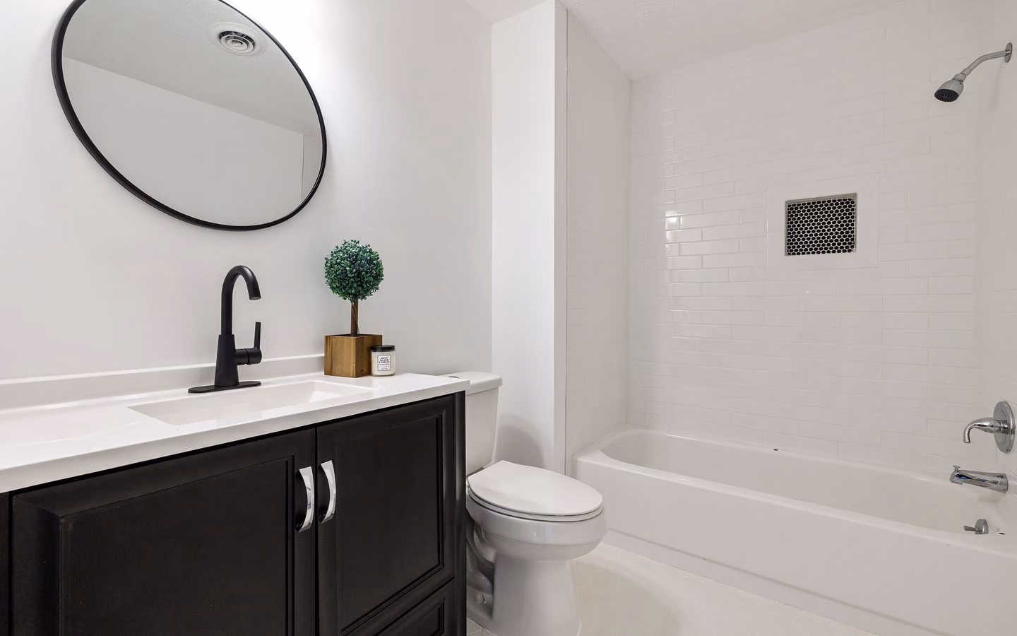 Bright minimalist bathroom with a white tub, black fixtures, and compact vanity storage