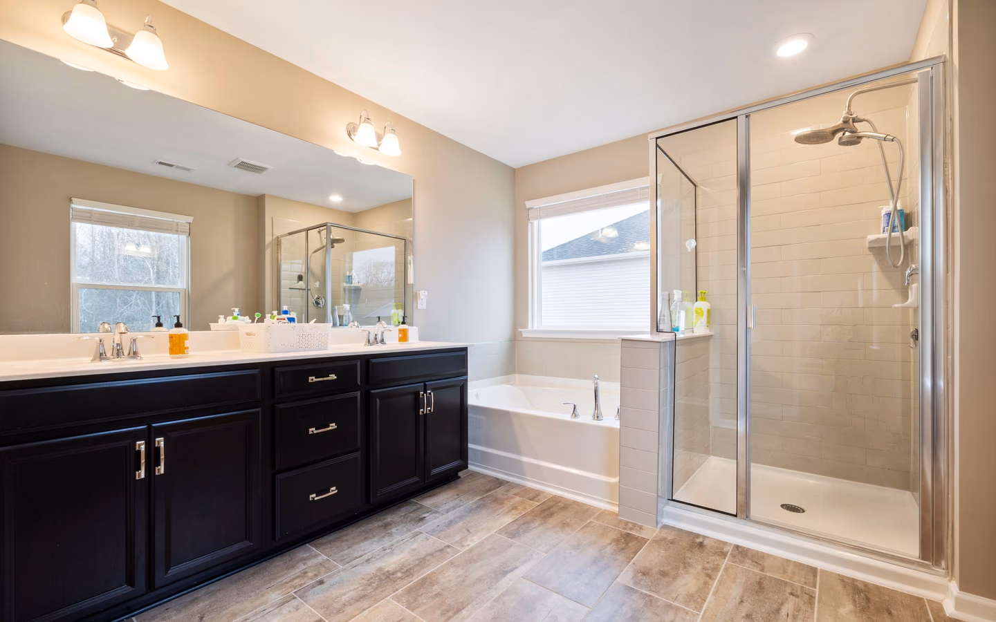 Spacious bathroom with a dark double vanity, bathtub, glass shower, and natural light