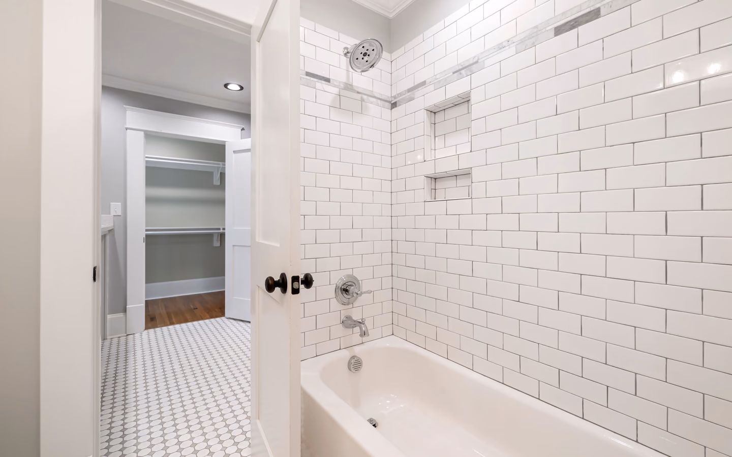 Bright bathroom with a tiled bathtub, built-in shelves, and an adjacent dressing area