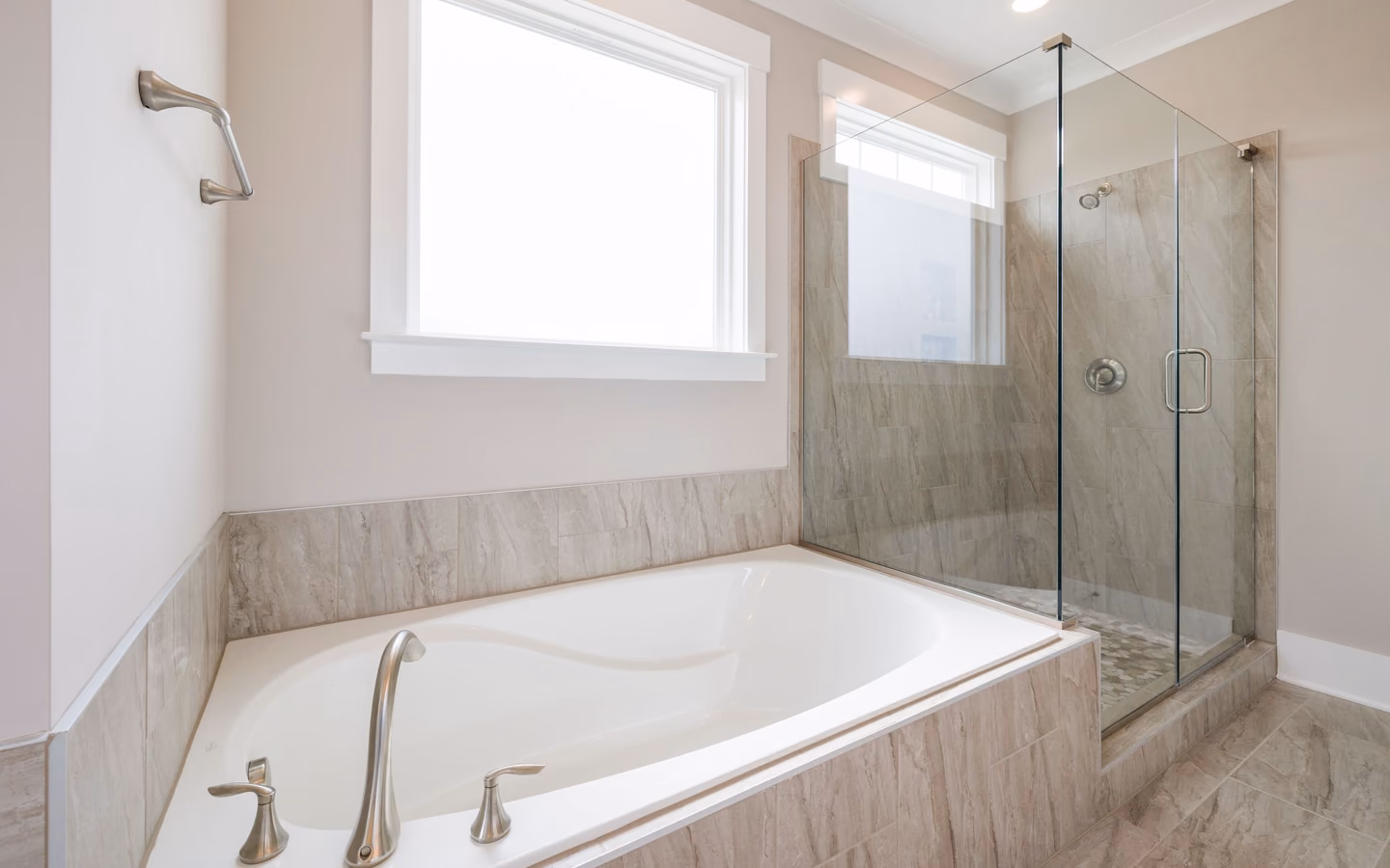 Bright guest bathroom with a white tub, glass shower screen, and marble-look finishes