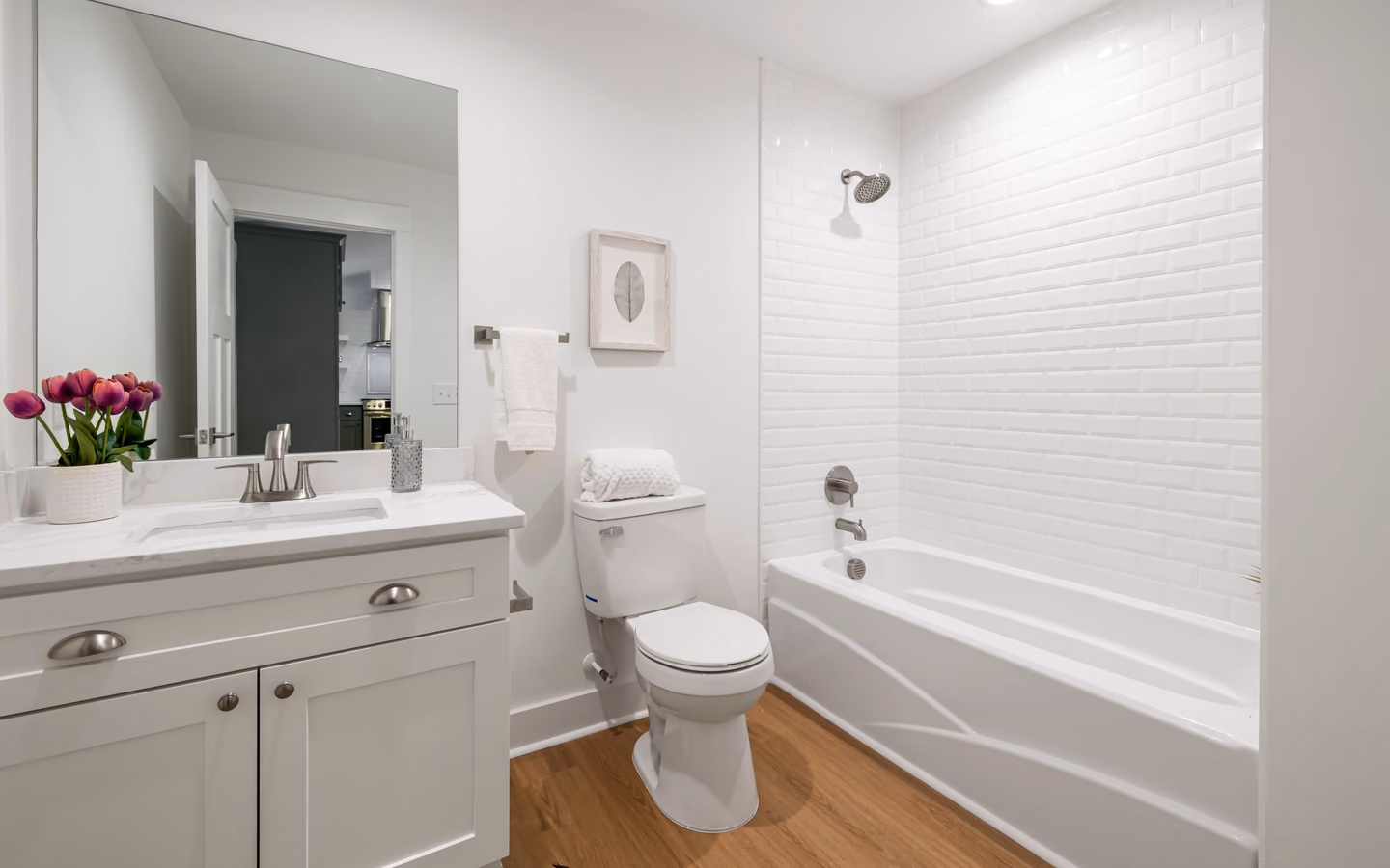 Bright minimalist bathroom with a white bathtub, sleek vanity, and warm wood flooring