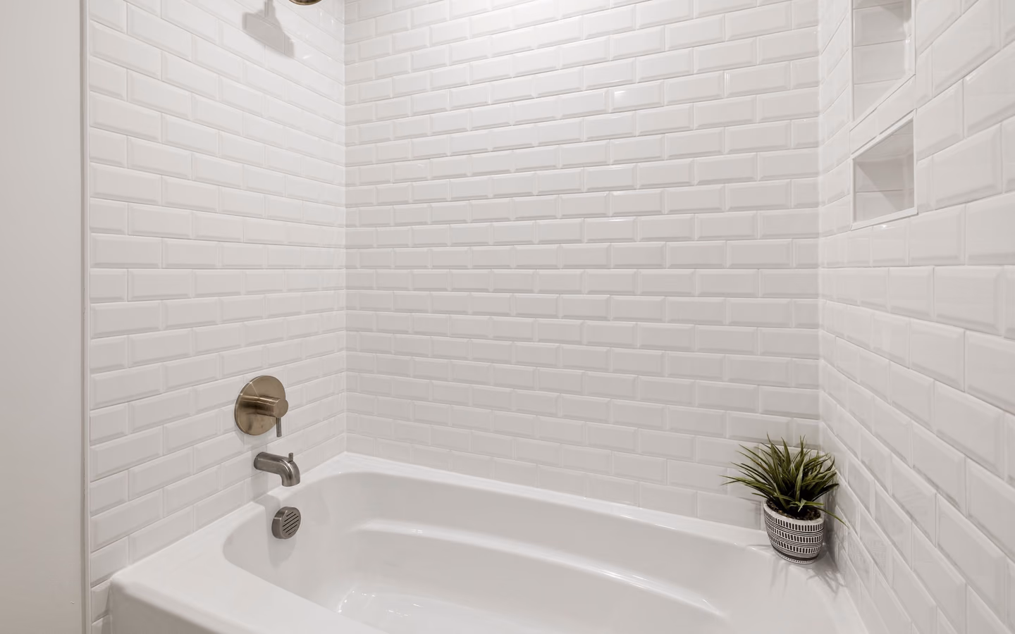 White subway-tile bathroom with a bathtub, plant accent, and simple modern fixtures