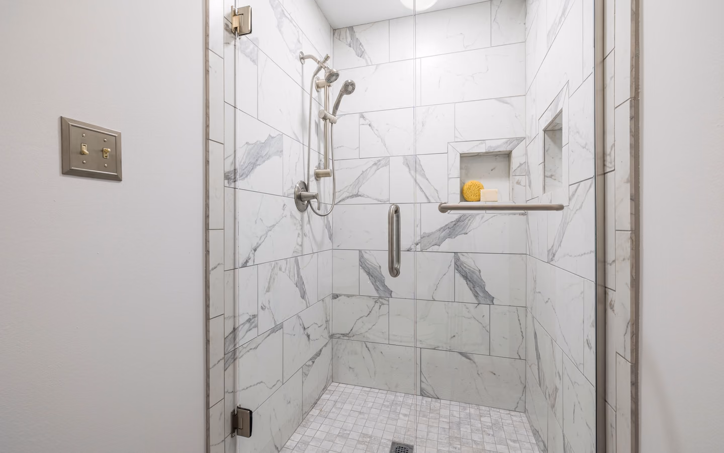 Spa-like walk-in shower finished in bright marble tile with clear glass and built-in storage