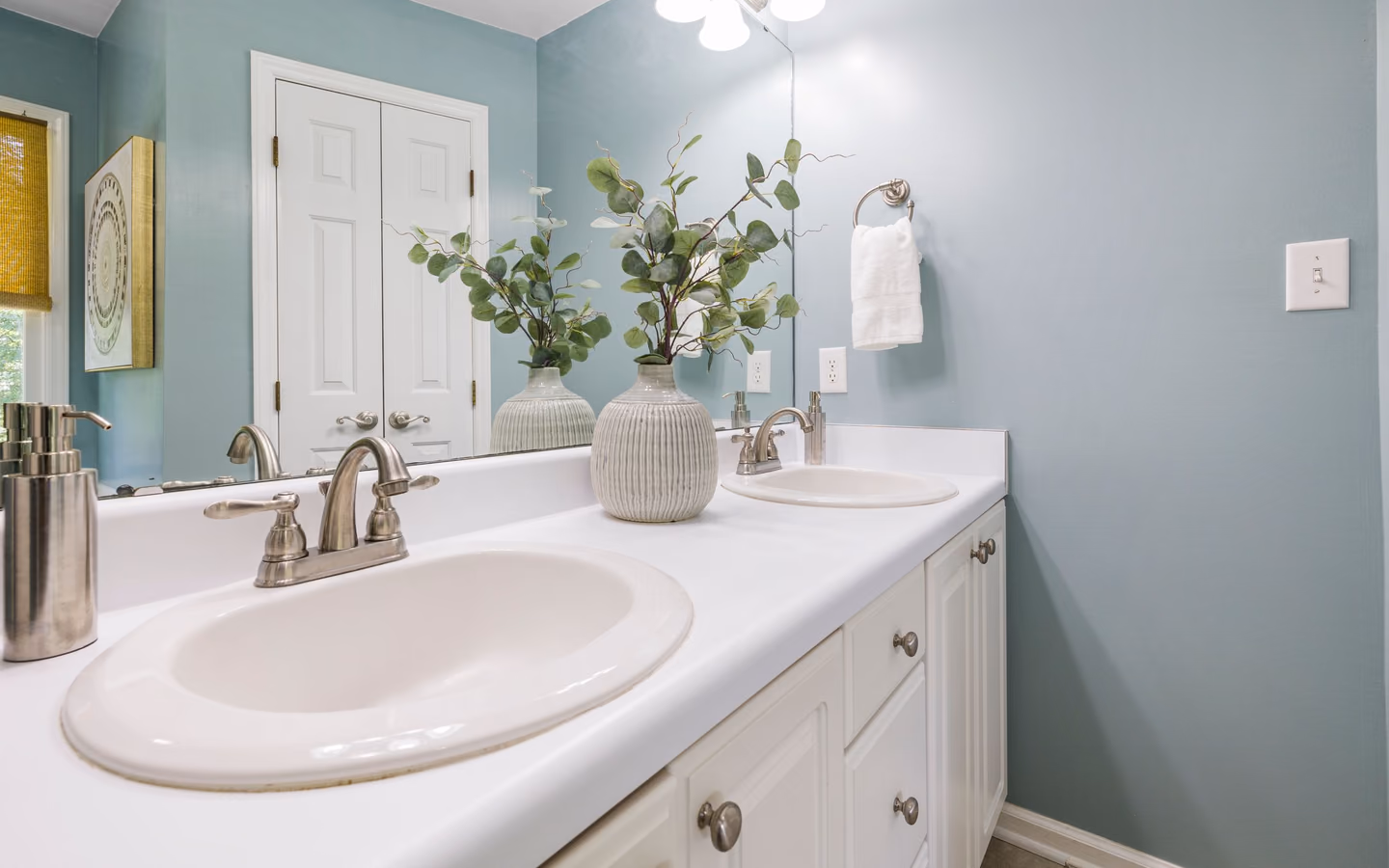 Bright contemporary bathroom with twin sinks, pale blue walls, and minimalist decor